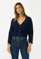 [Color: Navy] A front facing image of a brunette model wearing a navy cropped knit cardigan with sequins and a button front. 