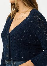 [Color: Navy] A detail image of a brunette model wearing a navy cropped knit cardigan with sequins and a button front. 