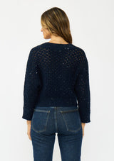[Color: Navy] A back facing image of a brunette model wearing a navy cropped knit cardigan with sequins and a button front. 