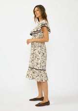 [Color: Natural/Olive] A side facing image of a brunette model wearing a beige and black floral print midi dress with short flutter sleeves, a v neckline, and a ruffle trimmed hem. 
