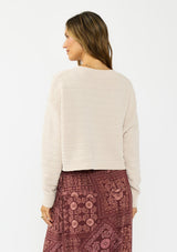 [Color: Birch] A back facing image of a brunette model wearing an off white chenille sweater with a round neck and long sleeves with dropped shoulders. Styled with the burgundy paisley  bohemian maxi skirt. 