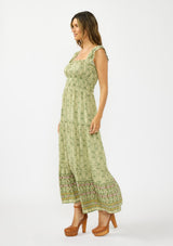 [Color: Olive/Rose] A side facing image of a brunette model wearing a green bohemian floral maxi dress with cap sleeves, a square neckline, elastic waist, and a tiered skirt with ruffle trims.