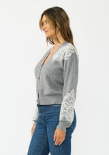[Color: Heather Grey] A side facing image of a brunette model wearing a grey cardigan with lace details, a v neckline, and a button front. 