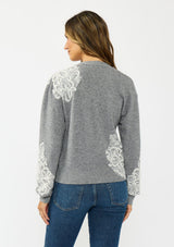 [Color: Heather Grey] A back facing image of a brunette model wearing a grey cardigan with lace details, a v neckline, and a button front. 