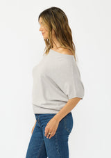 [Color: Light Heather Grey] A side facing image a brunette model wearing an off the shoulder sweater top with short sleeves and a fitted ribbed hem. 