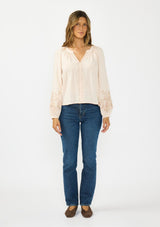 [Color: Petal] A front facing image  of a brunette model wearing a light pink embroidered blouse with a split v neckline. Styled with a dark wash denim and brown ballet flats. 