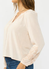 [Color: Petal] A detail image  of a brunette model wearing a light pink embroidered blouse with a split v neckline. 