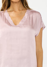 [Color: Dusty Orchid] A detail image of a brunette model wearing a pink satin top with an embroidered trim and short dolman sleeves. 