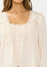 [Color: Petal] A detail image of a brunette model wearing an off white lace long sleeve top with a scoop neckline and button front. Styled with dark wash straight leg denim. 