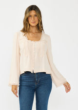 [Color: Petal] A front facing image of a brunette model wearing an off white lace long sleeve top with a scoop neckline and button front. 