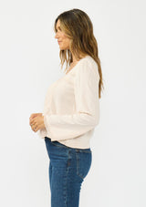 [Color: Petal] A side facing image of a brunette model wearing an off white lace long sleeve top with a scoop neckline and button front. Styled with dark wash straight leg denim. 