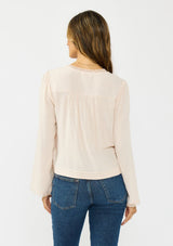 [Color: Petal] A back facing image of a brunette model wearing an off white lace long sleeve top with a scoop neckline and button front. Styled with dark wash straight leg denim. 