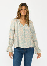 [Color: Dusty Sage/Natural] A front facing image of a brunette model wearing a mint floral blouse with a button front, long sleeves, flared elastic cuffs, and lace trims details. 