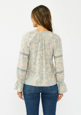 [Color: Dusty Sage/Natural] A back facing image of a brunette model wearing a mint floral blouse with a button front, long sleeves, flared elastic cuffs, and lace trims details. 