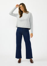[Color: Heather Silver] A front facing image of a brunette model wearing a grey pullover sweater with a crew neckline and a open back detail. Styled with a dark wash denim with patch pockets and loafers. 