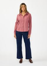 [Color: Rose] A front facing image of a brunette model wearing a pink shirt with a classic collar and button front. Styled with a dark wash denim with patch pockets and loafers. 