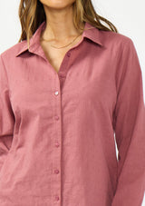 [Color: Rose] A detail image of a brunette model wearing a pink shirt with a classic collar and button front. 