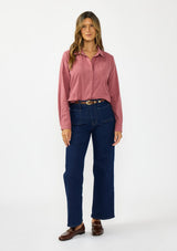 [Color: Rose] A front facing image of a brunette model wearing a pink shirt with a classic collar and button front. Styled with a dark wash denim with patch pockets and loafers. 