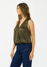 [Color: Olive] A side facing image of a brunette model wearing a olive green sleeveless top with an embroidered trim, elastic hem, and a surplice front. 