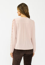 [Color: Shell] A back facing image of a brunette model wearing a pink embroidered top with mesh detail. Styled with a dark brown corduroy. 