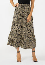 [Color: Black/Natural] A front facing image of a model wearing a tan and lack boho skirt with a tiered ruffle hem. Styled with black strappy heels. 