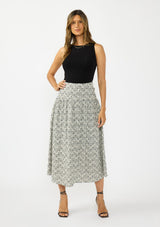 [Color: Black] A front facing image of an brunette model wearing a black tank top with a black and white embroidered checkered  midi skirt with a side zipper. 