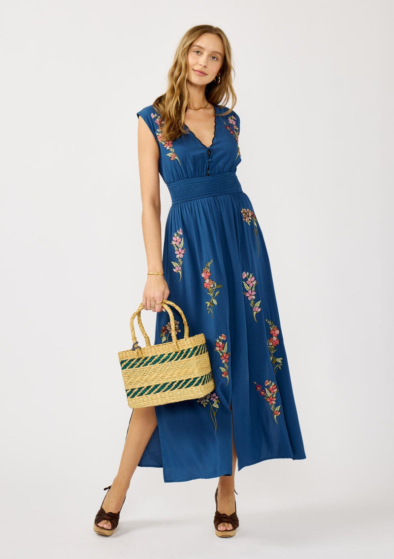 [Color: Navy] A front facing image of a blonde model wearing a blue embroidered maxi dress with w scalloped v-neckline, a smocked waist, and slits. A flowy summer dress for garden parties and soirees. 