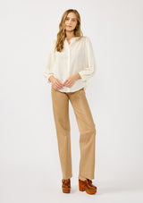 [Color: Cream] A front facing image of a blonde model wearing an ivory button front top with a high ruffled neckline, long sleeves, and smocked elastic cuffs. A relaxed fit blouse perfect for the office and special occasions. 