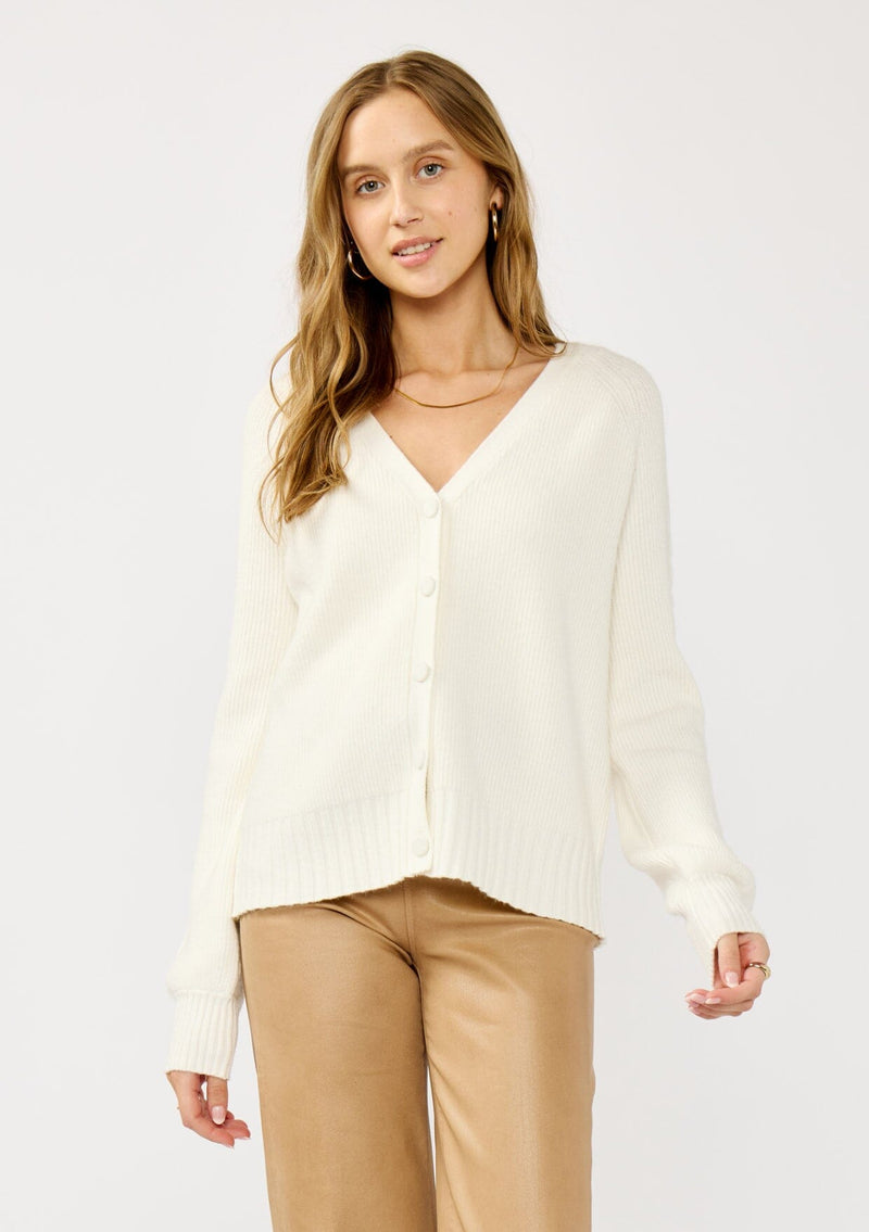 [Color: White] A front facing image of a blonde model wearing a white cozy rib stitch cardigan with a button front, v-neckline, ribbed border, and cable knit detailing along the sleeves. 