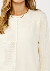 [Color: Cloud] A detail image of a blonde model wearing a white cozy mix knit pullover sweater with a classic crew neckline. Lightweight and warm for casual outings or the office. 