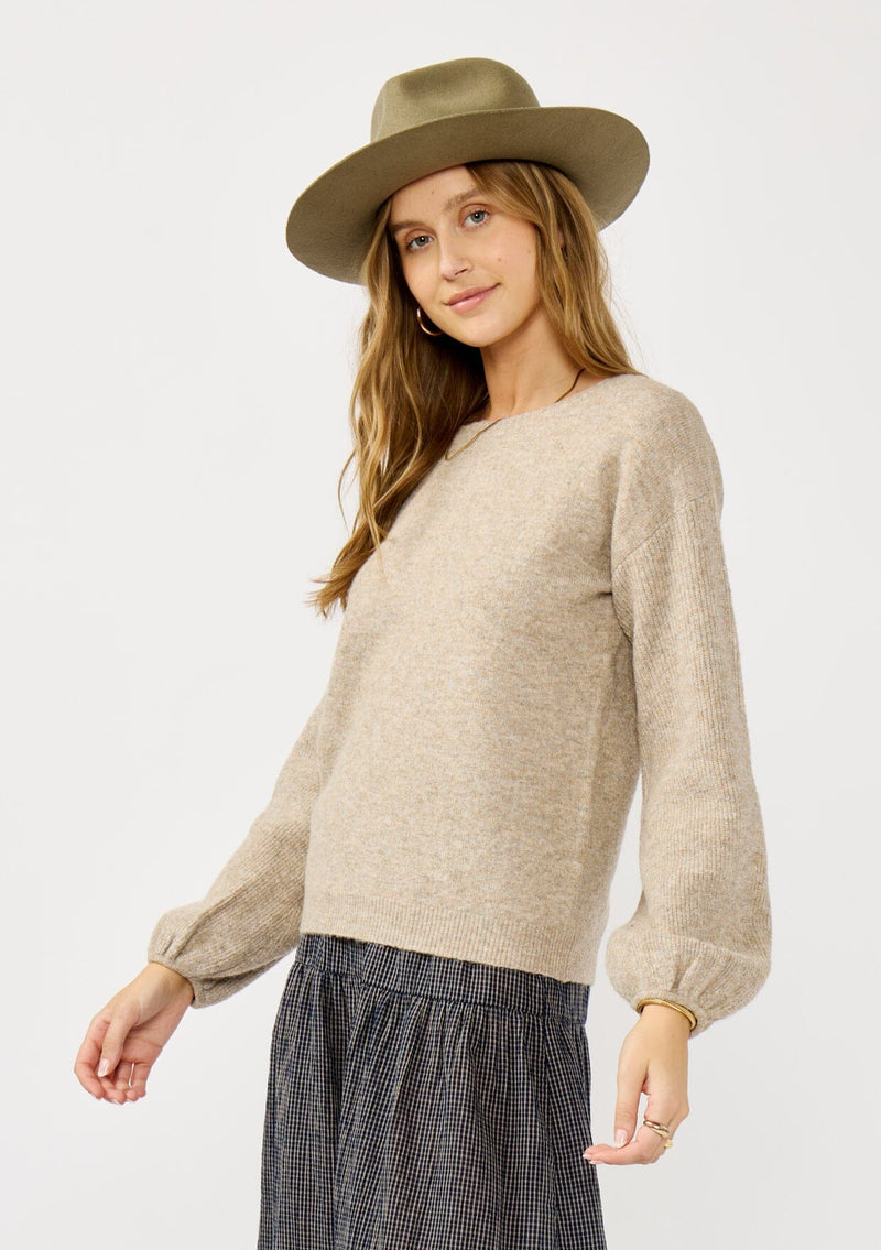 [Color: Heather Cement] A side facing image of a blonde model in a beige crewneck pullover sweater with ribbed blouson sleeves. A versatile knit ideal for styling with skirts or trousers for a chic, polished outfit.