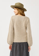 [Color: Heather Cement] A back facing image of a blonde model in a beige crewneck pullover sweater with ribbed blouson sleeves. A versatile knit ideal for styling with skirts or trousers for a chic, polished outfit.