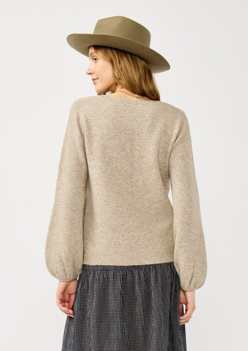 [Color: Heather Cement] A back facing image of a blonde model in a beige crewneck pullover sweater with ribbed blouson sleeves. A versatile knit ideal for styling with skirts or trousers for a chic, polished outfit.