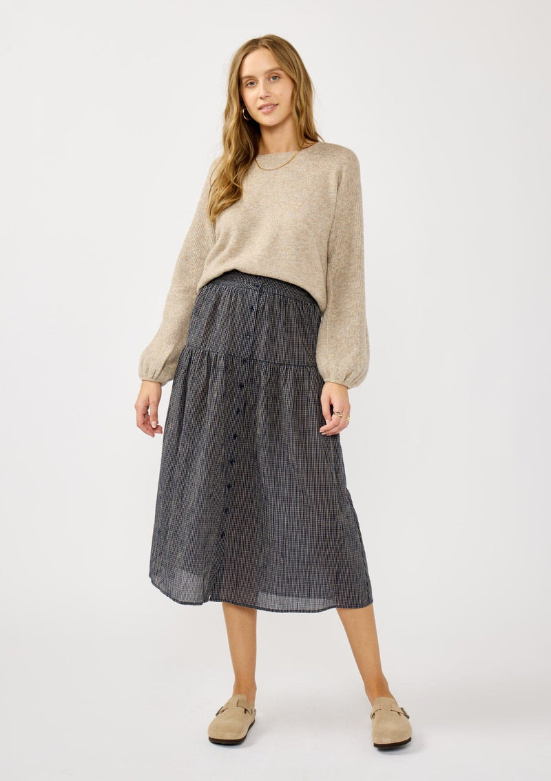 [Color: Navy/Taupe] A front facing image of a blonde model wearing a navy gingham skit with a button front and a smocked elastic waist at the back. A boho fall skirt paired with a sweater for the fall season. 