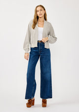 [Color: Heather Light Grey] A front facing image of a blonde model wearing a grey casual, lightweight cardigan with an open front, ribbed trim, and rolled edges. A classic staple cardigan for transitional styling. 