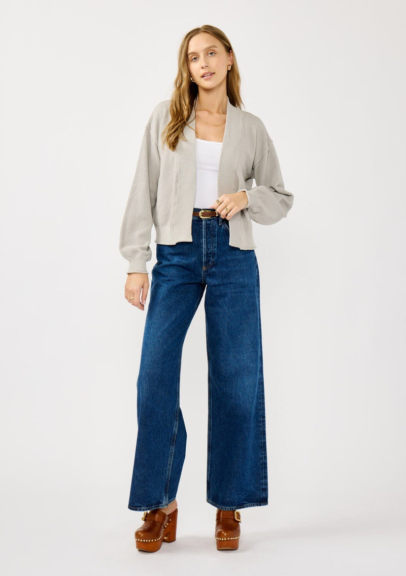 [Color: Heather Light Grey] A front facing image of a blonde model wearing a grey casual, lightweight cardigan with an open front, ribbed trim, and rolled edges. A classic staple cardigan for transitional styling. 