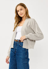 [Color: Heather Light Grey] A front facing image of a blonde model wearing a grey casual, lightweight cardigan with an open front, ribbed trim, and rolled edges. A classic staple cardigan for transitional styling. 