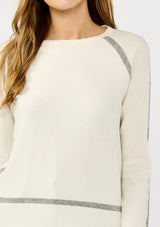 [Color: Cream/Heather Grey] A detail image of a blonde model wearing a cream pullover sweater with a grey border stripe. Featuring long cozy sleeves, a classic crew neckline, and ribbed trimming. 