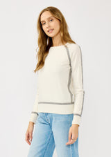 [Color: Cream/Heather Grey] A side facing image of a blonde model wearing a cream pullover sweater with a grey border stripe. Featuring long cozy sleeves, a classic crew neckline, and ribbed trimming. 