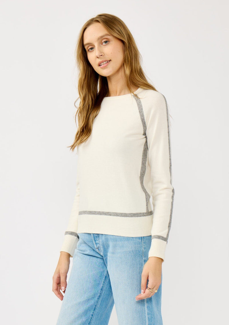 [Color: Cream/Heather Grey] A side facing image of a blonde model wearing a cream pullover sweater with a grey border stripe. Featuring long cozy sleeves, a classic crew neckline, and ribbed trimming. 