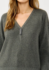 [Color: Heather Charcoal] A detail image of a blonde model wearing a dark grey pullover sweater with a unique suede accent at the v-neckline. 