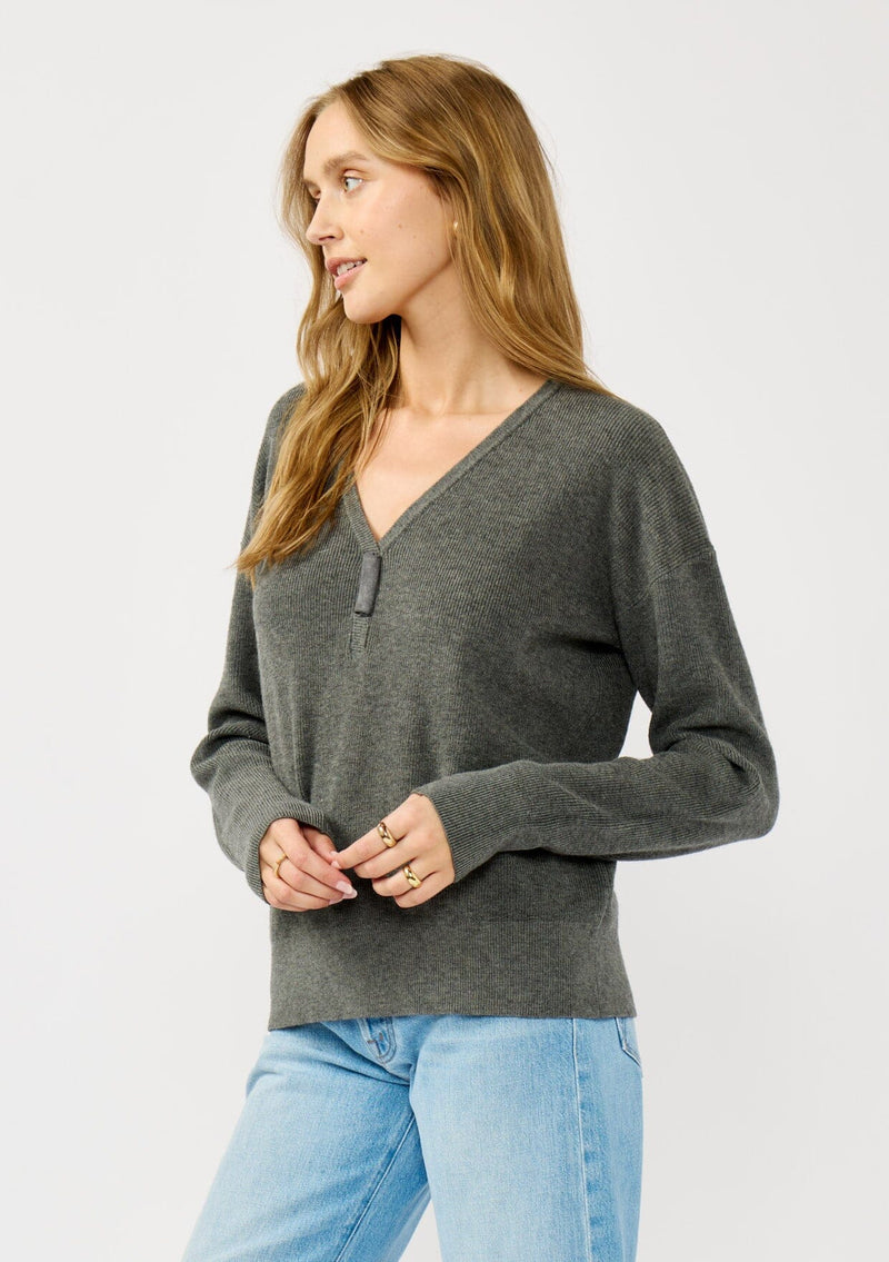 [Color: Heather Charcoal] A side facing image of a blonde model wearing a dark grey pullover sweater with a unique suede accent at the v-neckline. 