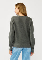 [Color: Heather Charcoal] A back facing image of a blonde model wearing a dark grey pullover sweater with a unique suede accent at the v-neckline. 