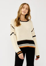 [Color: Natural/Black] A front facing image of a blonde model wearing a cotton pointelle knit sweater with a border stripe. Featuring a classic crew neckline, dropped shoulders, and open knit details along the sleeves. 