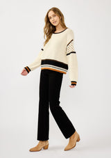 [Color: Natural/Black] A side facing image of a blonde model wearing a cotton pointelle knit sweater with a border stripe. Featuring a classic crew neckline, dropped shoulders, and open knit details along the sleeves. 