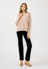 [Color: Heather Oat] A front facing image of a blonde model wearing a light brown pullover crew neck sweater with ribbed accents, side vents, and a high low hemline. 