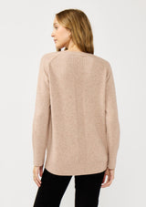 [Color: Heather Oat] A back facing image of a blonde model wearing a light brown pullover crew neck sweater with ribbed accents, side vents, and a high low hemline. 