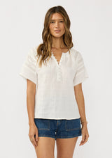 [Color: Off White] A front facing image of a brunette model wearing a white cotton gauze top top with lace details on the sleeves and a half button front. 