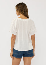 [Color: Off White] A back facing image of a brunette model wearing a white cotton gauze top top with lace details on the sleeves and a half button front. 