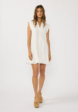[Color: White] A front facing image f a brunette model earing a white baby doll mini dress an eyelet design, split v-neckline, button front, and rolled cap sleeves. 